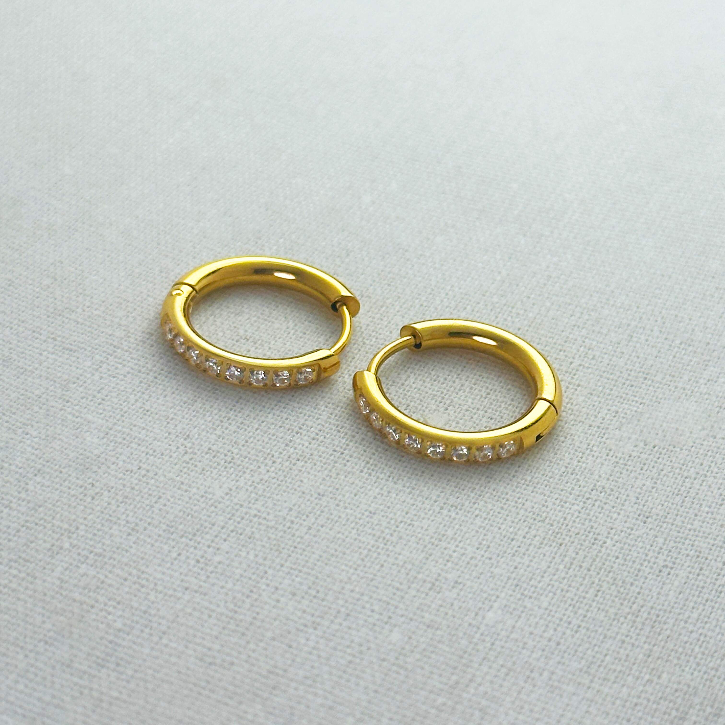 Gold hoop earrings with embedded stones on a light gray background