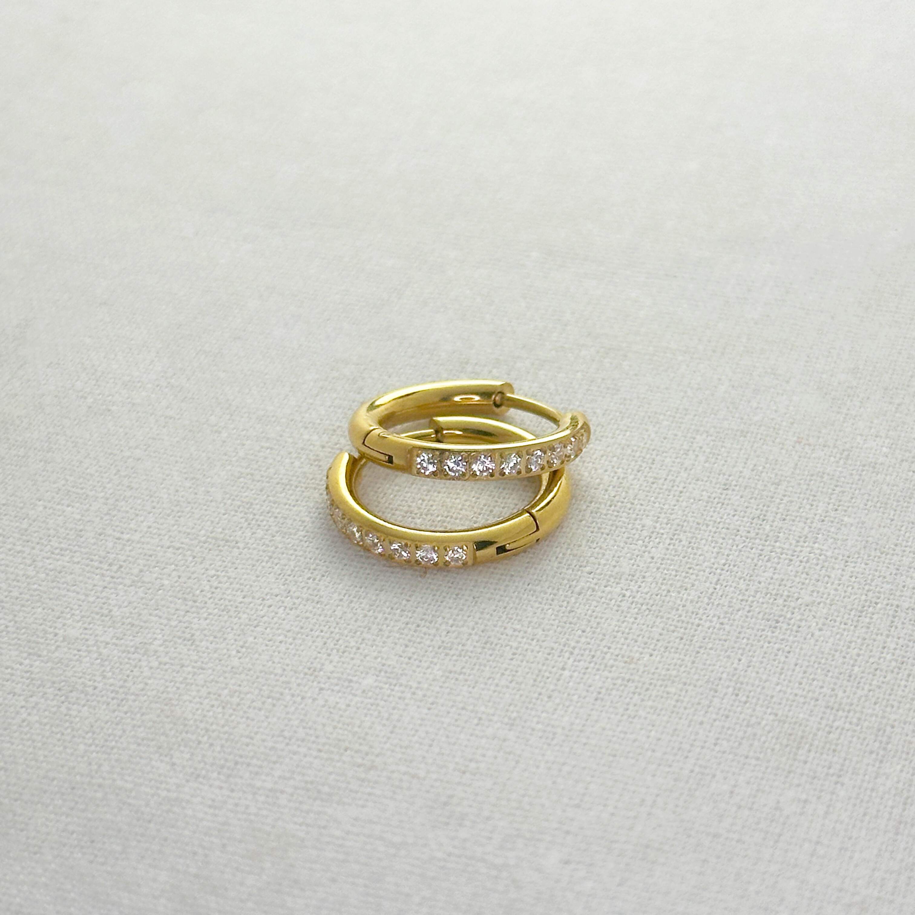 Gold hoop earrings with embedded diamonds on a light gray background
