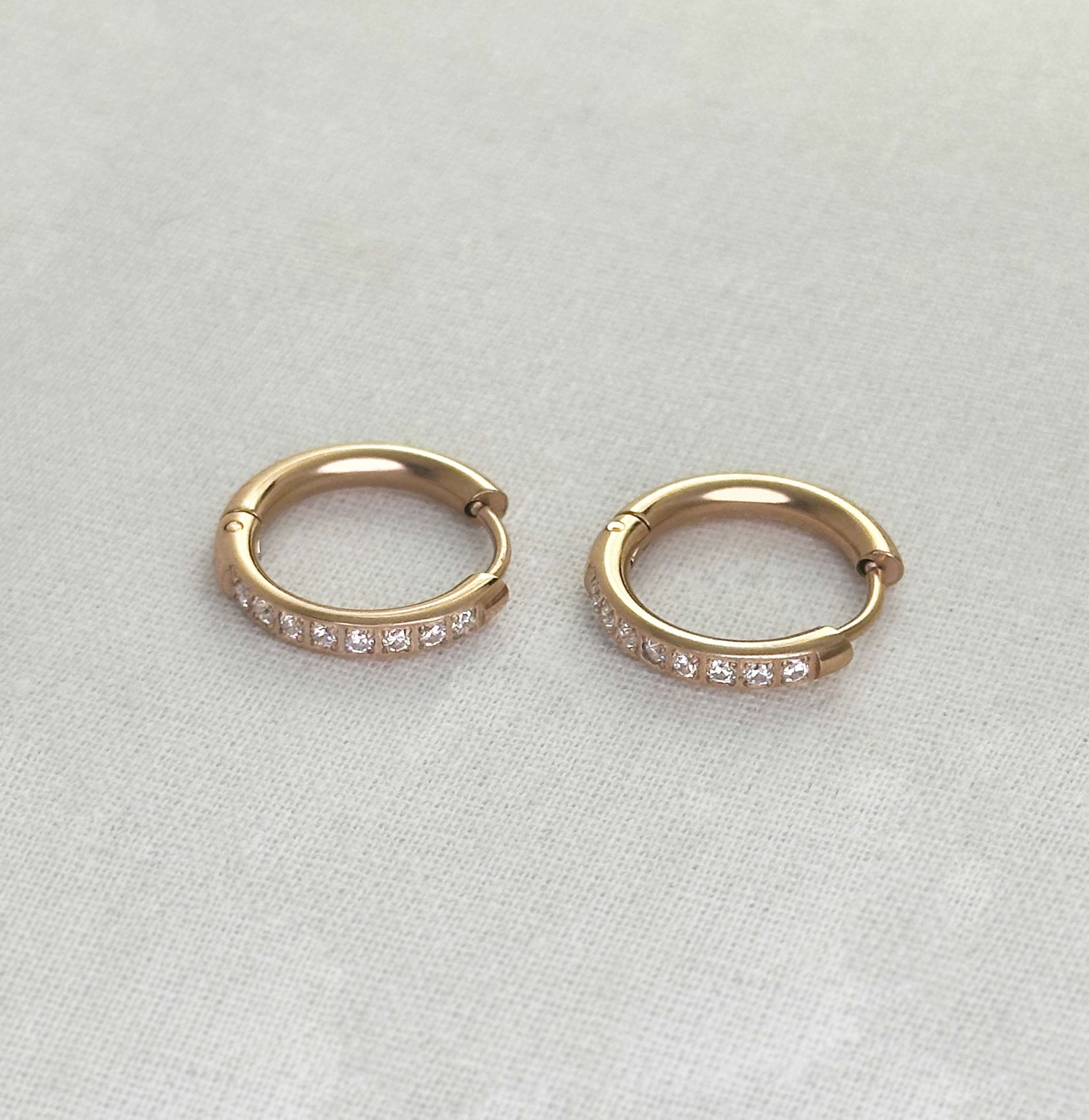 Pair of rose gold hoop earrings with small diamonds on a light gray background