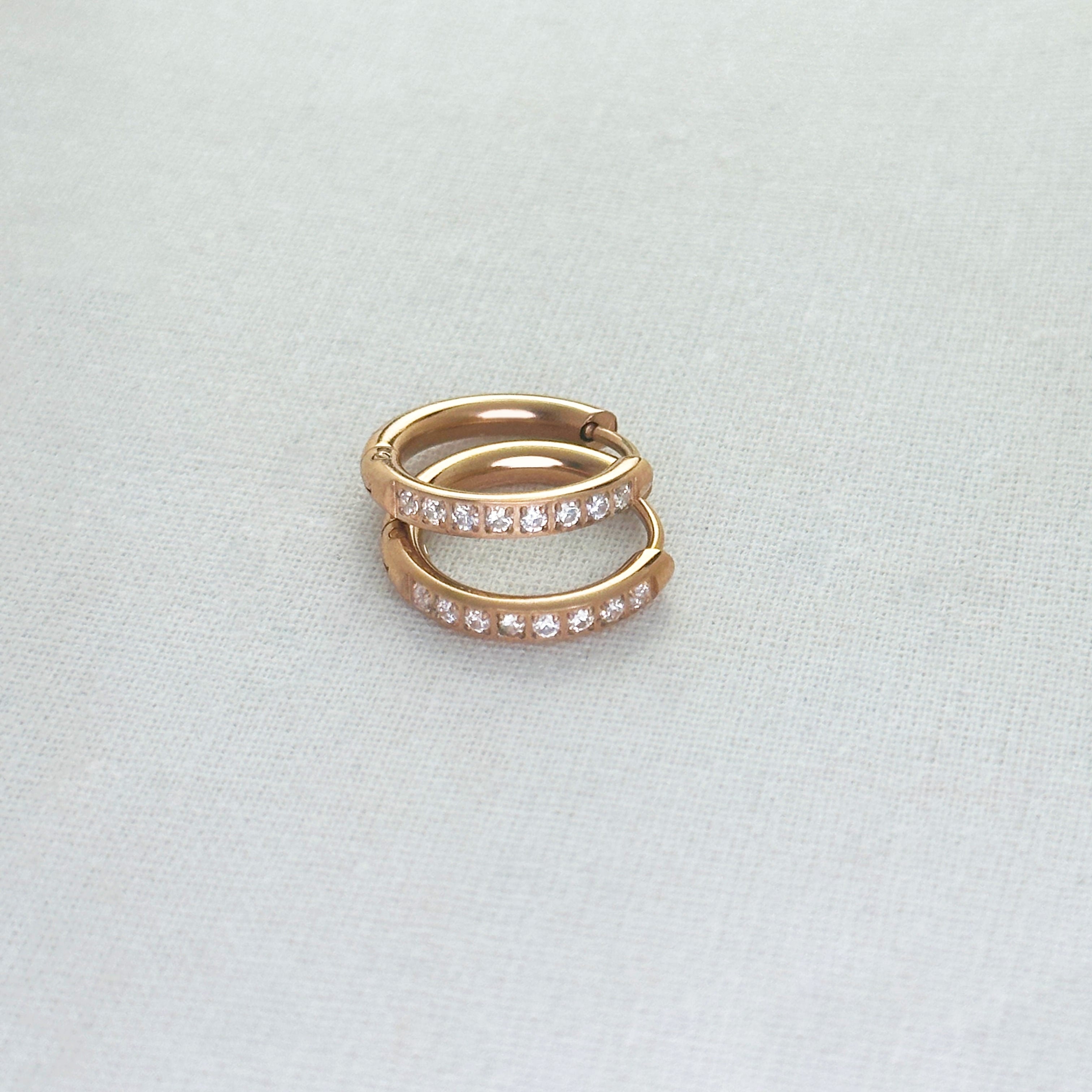 Pair of rose gold hoop earrings with embedded stones on a light gray background