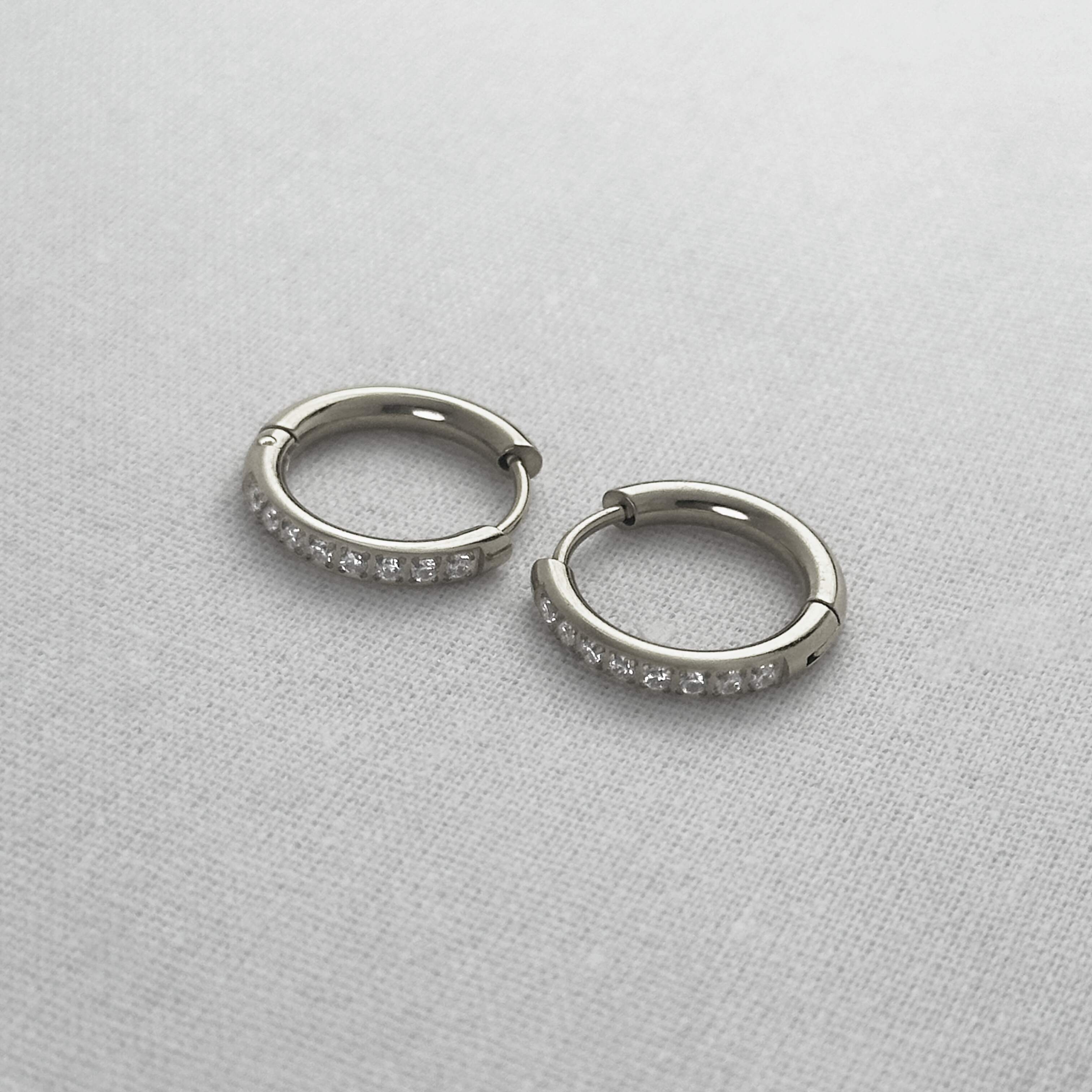 Pair of silver hoop earrings with small stones on a light gray background