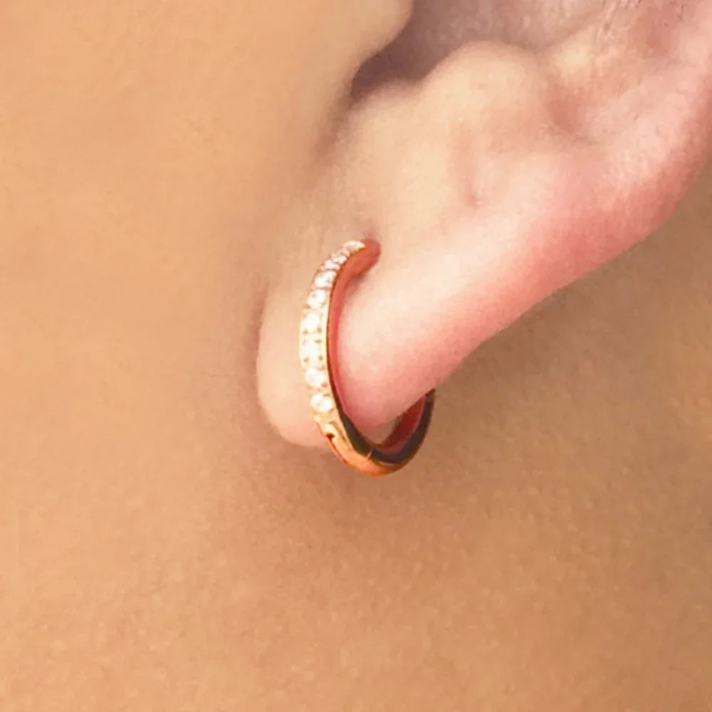 Rose gold hoop earring worn on a person's ear with a soft beige background