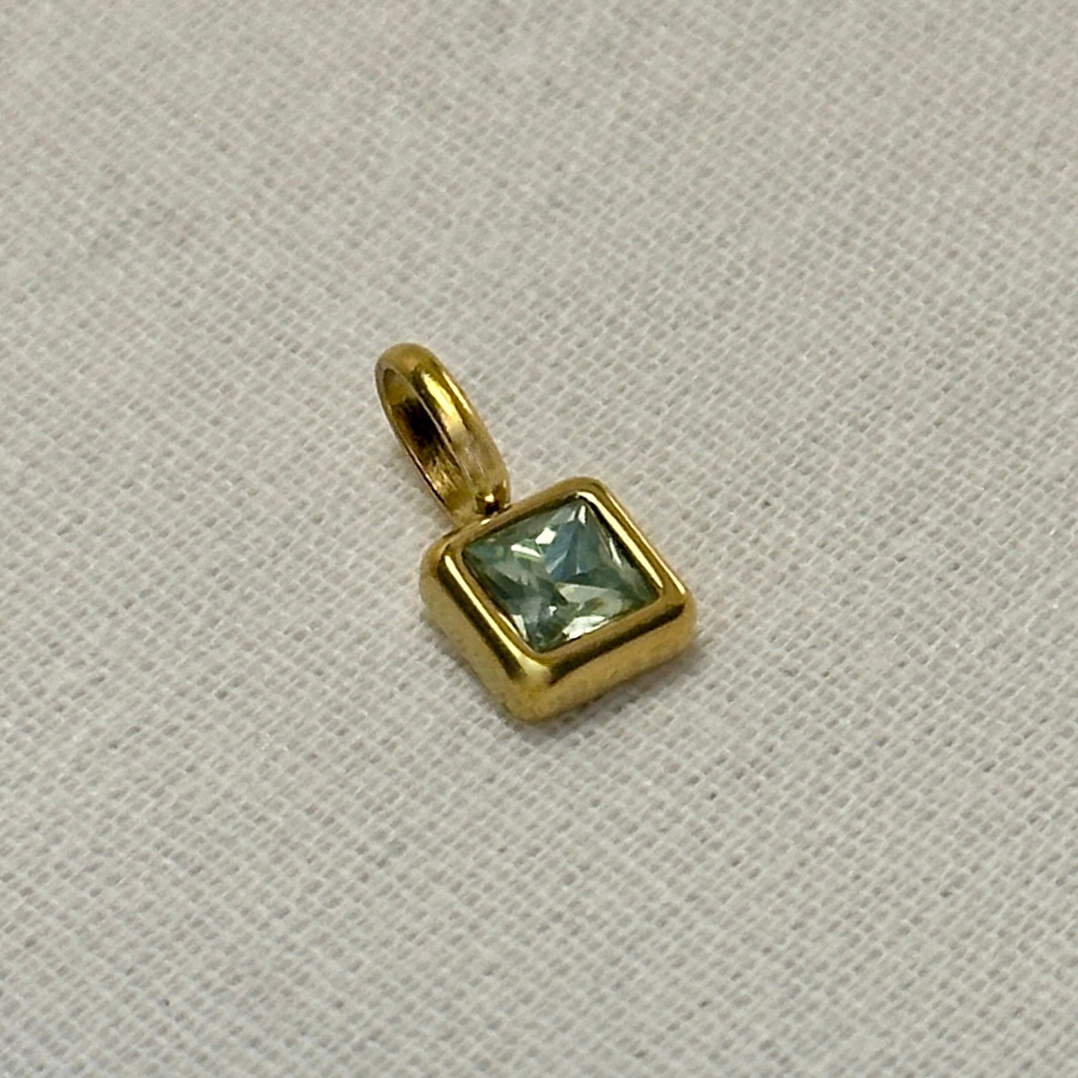 Gold pendant with a green gemstone on a light gray background