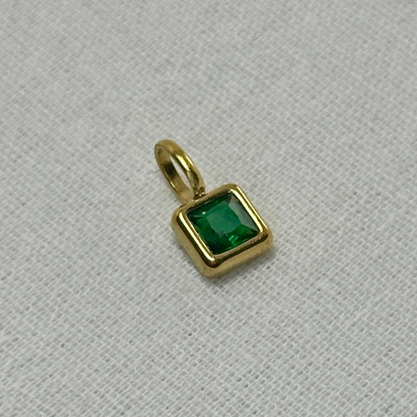 Gold pendant with a green gemstone on a light gray background