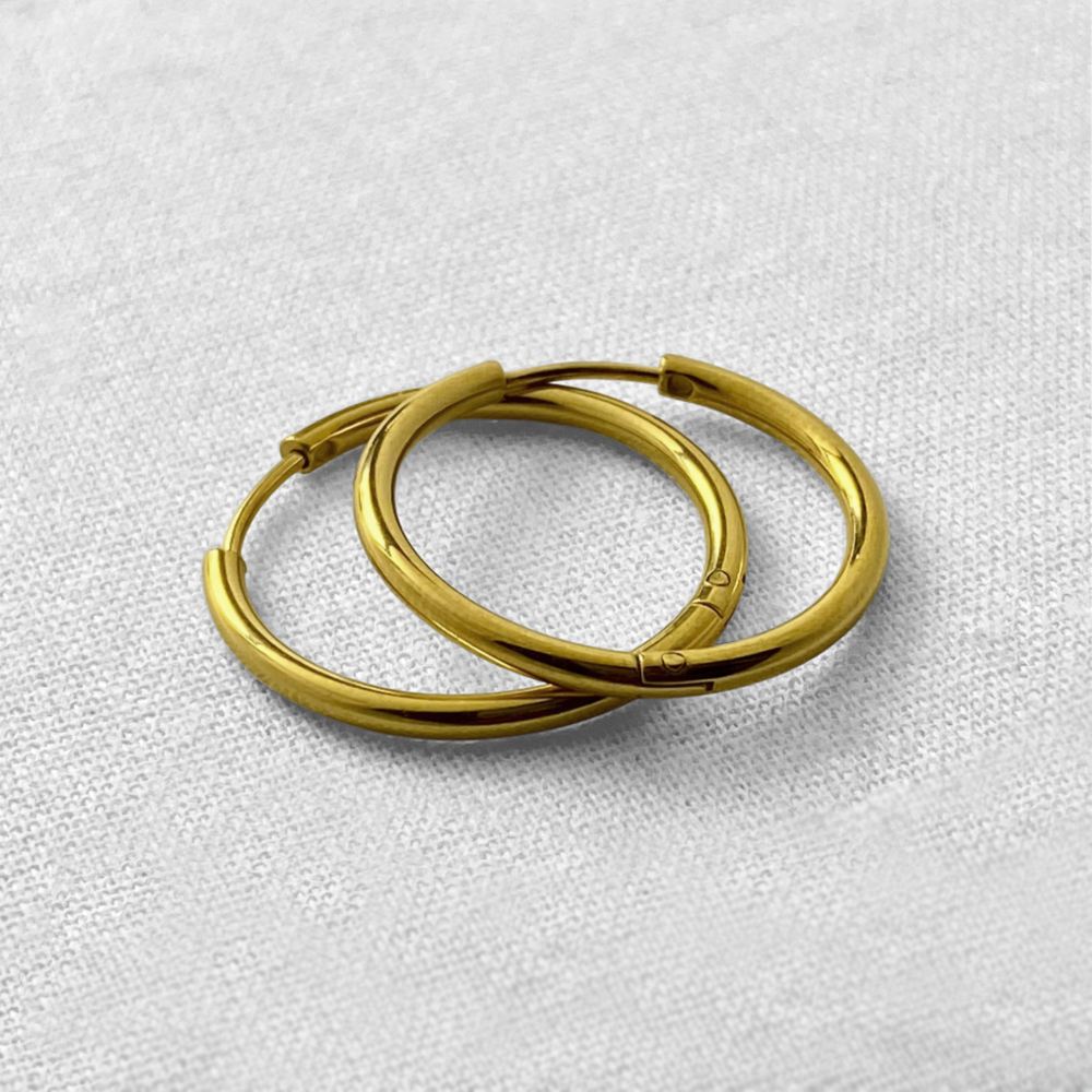 Two gold hoop earrings on a light gray textured background