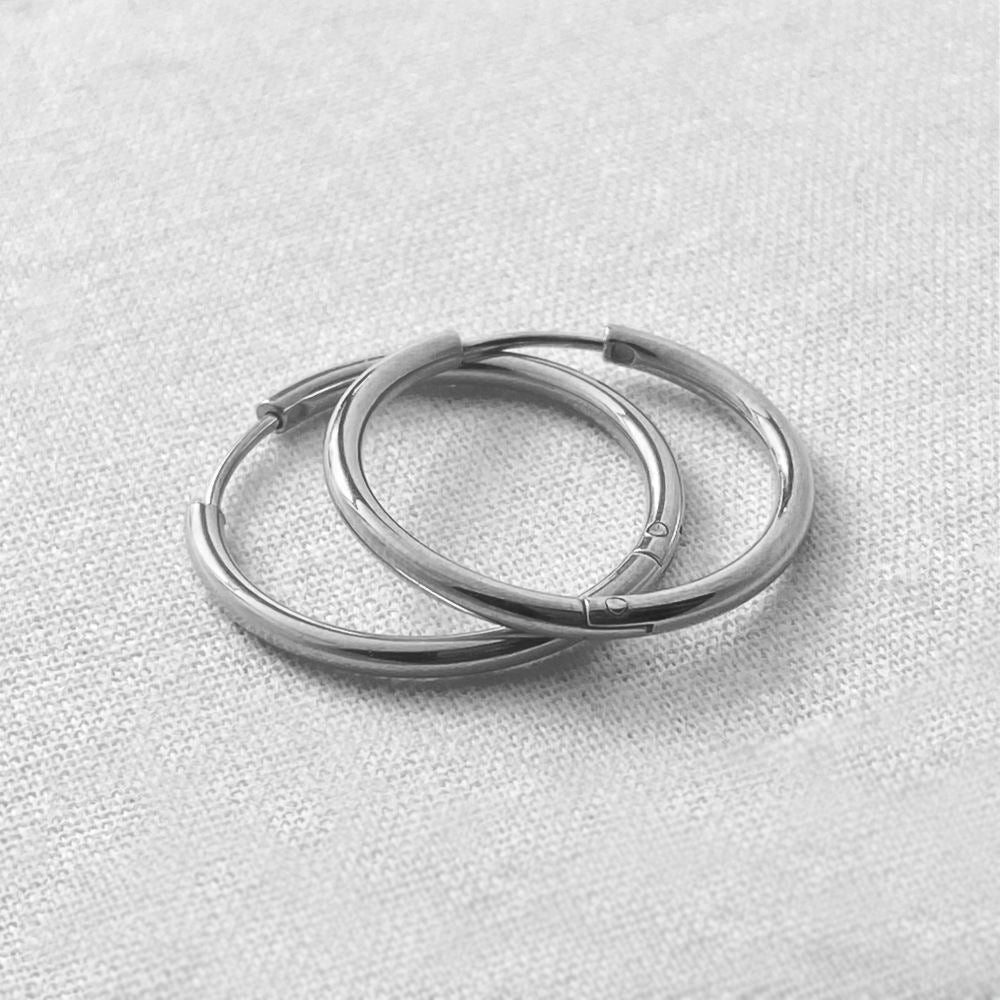 Two silver hoop earrings on a light gray textured background