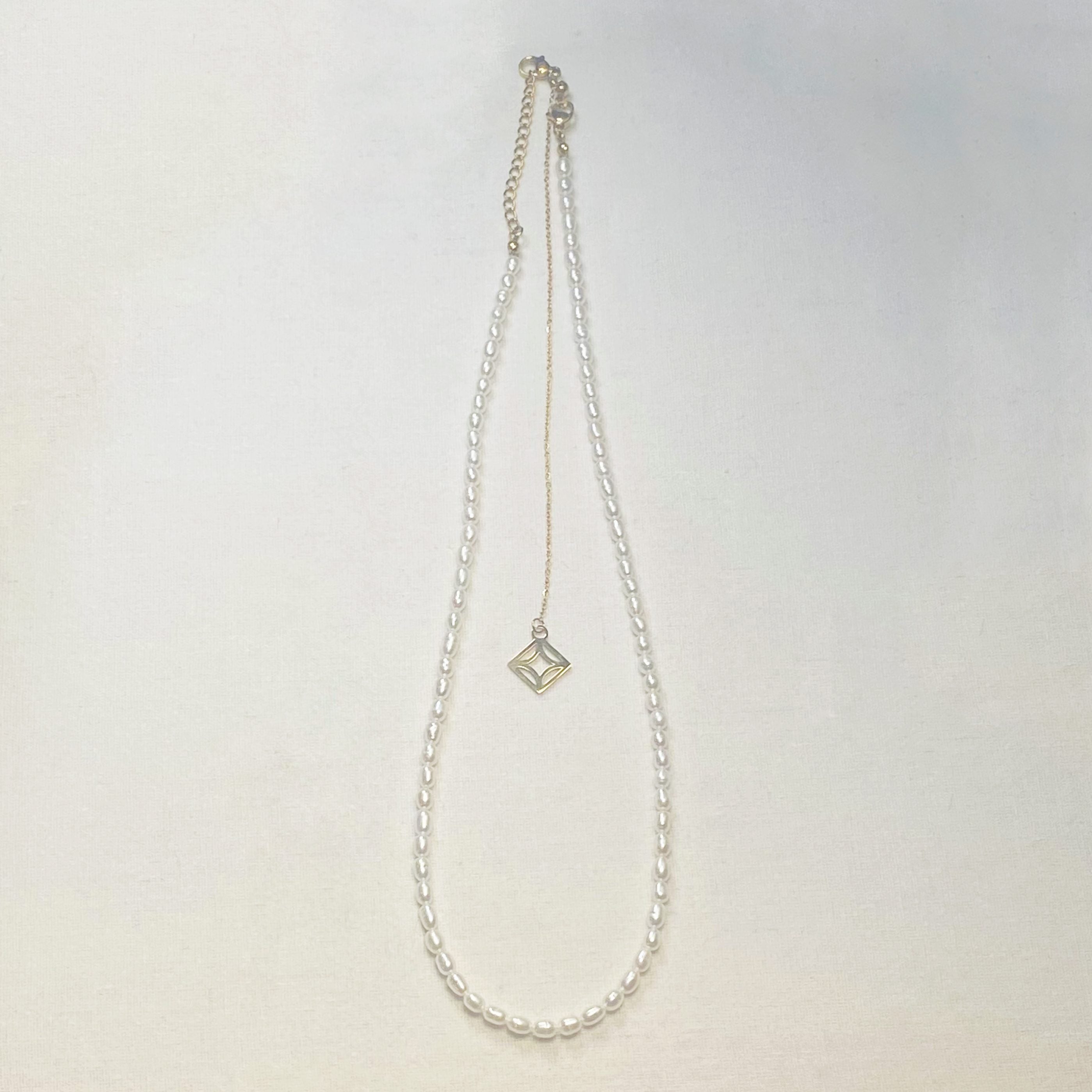 Pearl necklace with a geometric gold pendant on a light gray background and lumenaura jewellery 