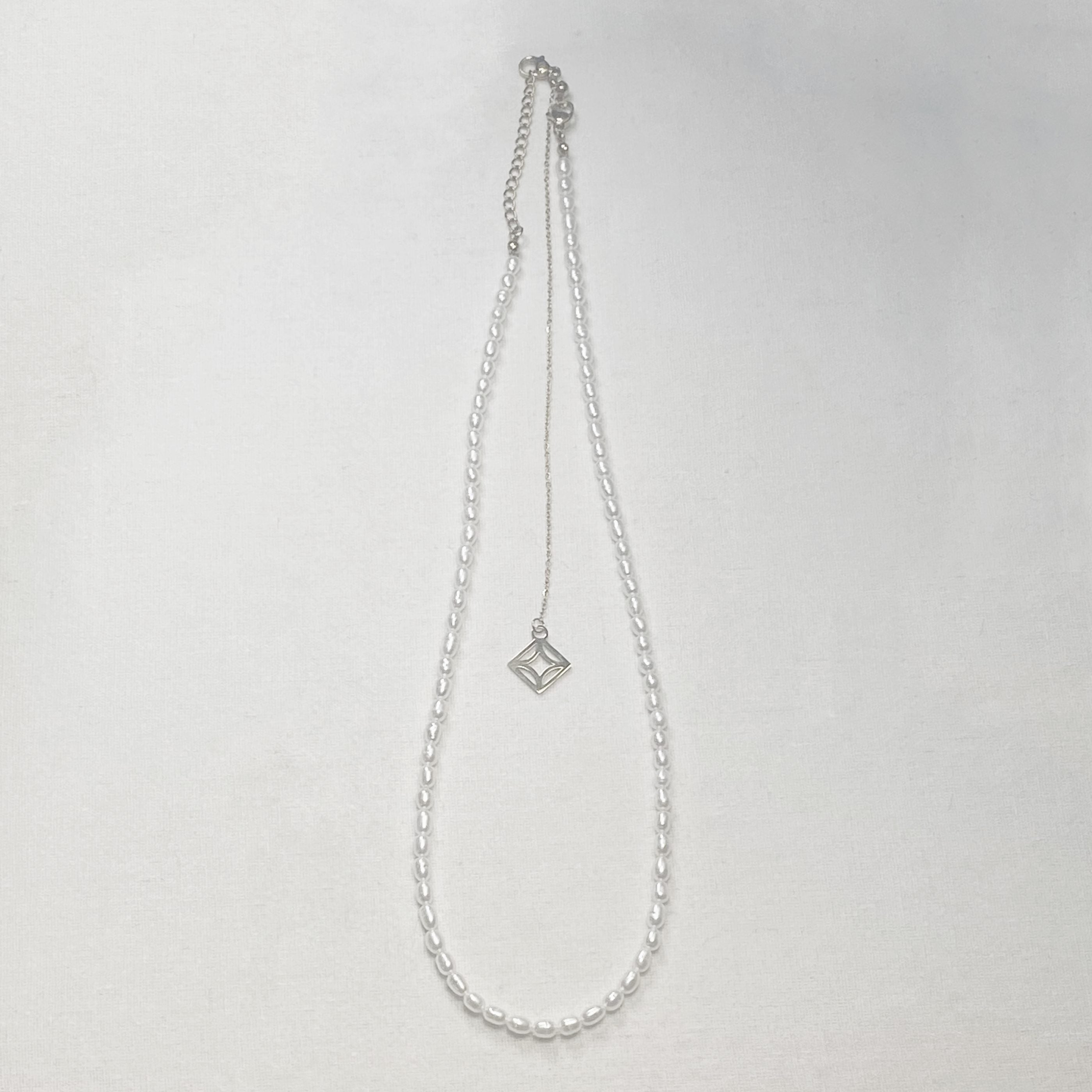 Silver necklace with a geometric silver pendant on a light gray background and lumenaura jewellery 