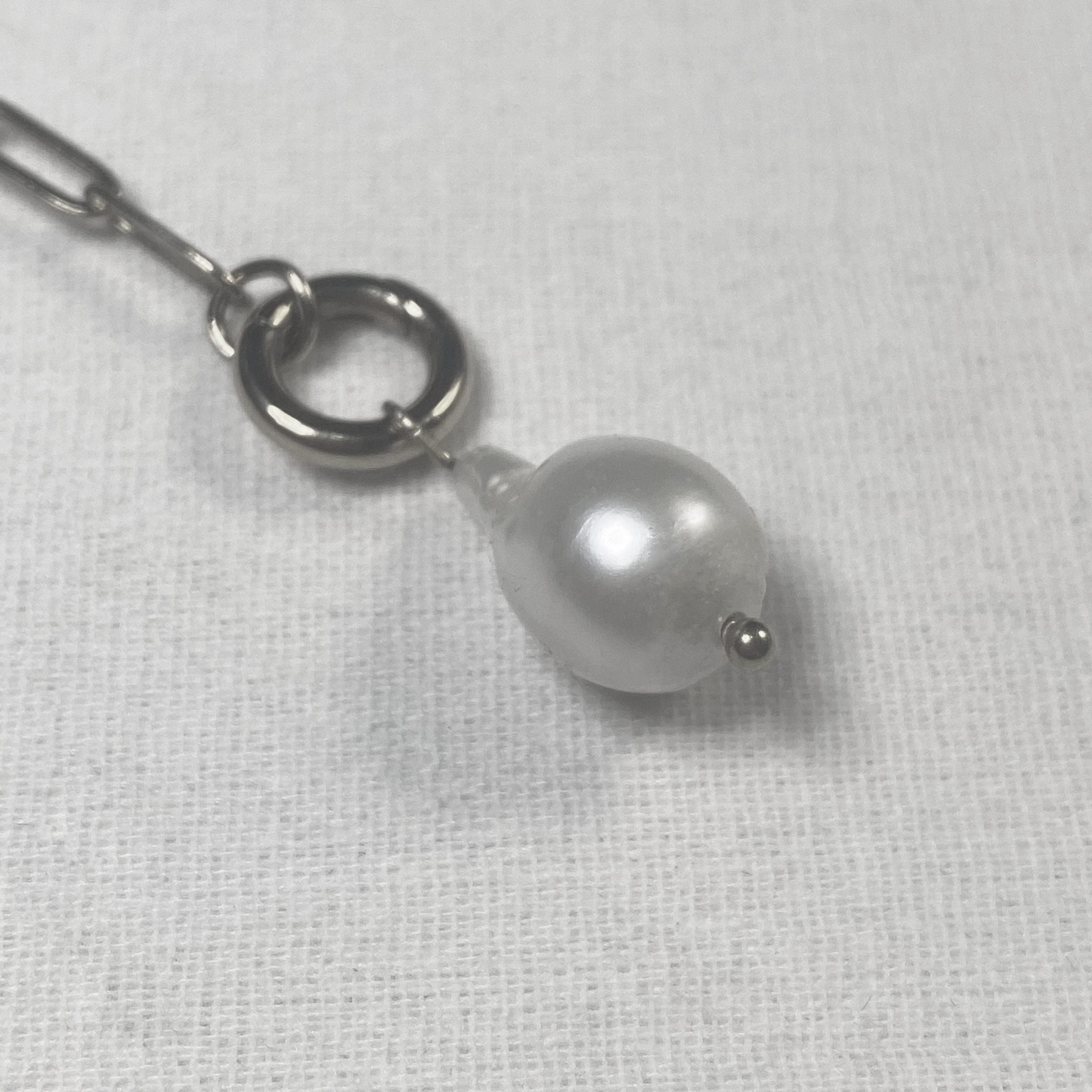 Pearl charm on a silver chain against a white fabric background and lumenaura jewellery 