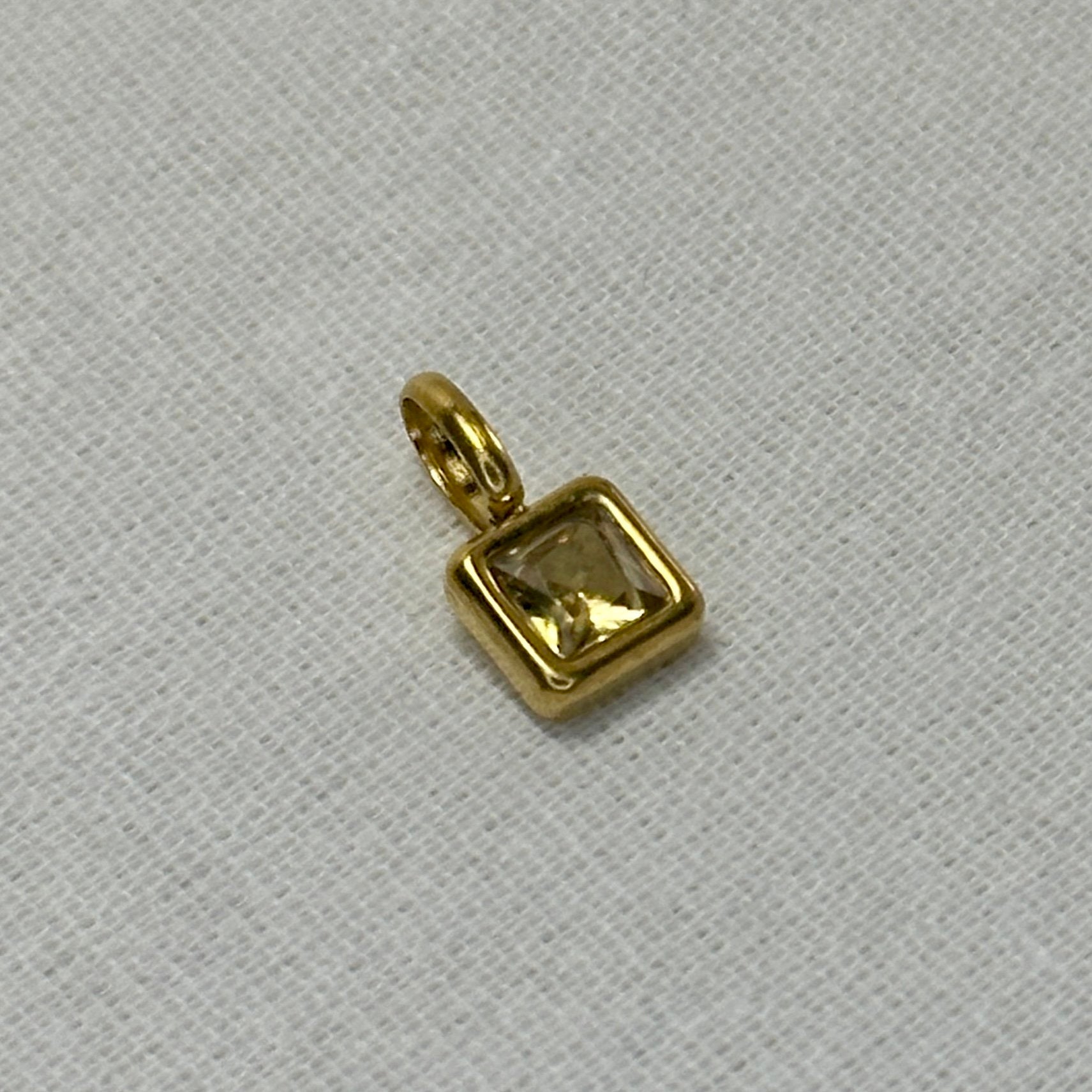 Gold pendant with a clear gemstone on a light gray background