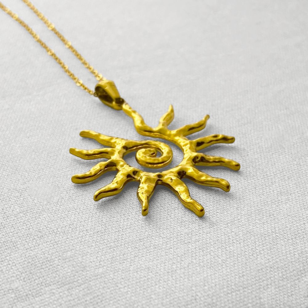 Gold sun-shaped pendant on a beige fabric background