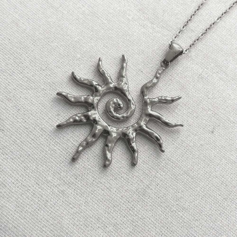 Silver sun-shaped pendant necklace on a light gray fabric background