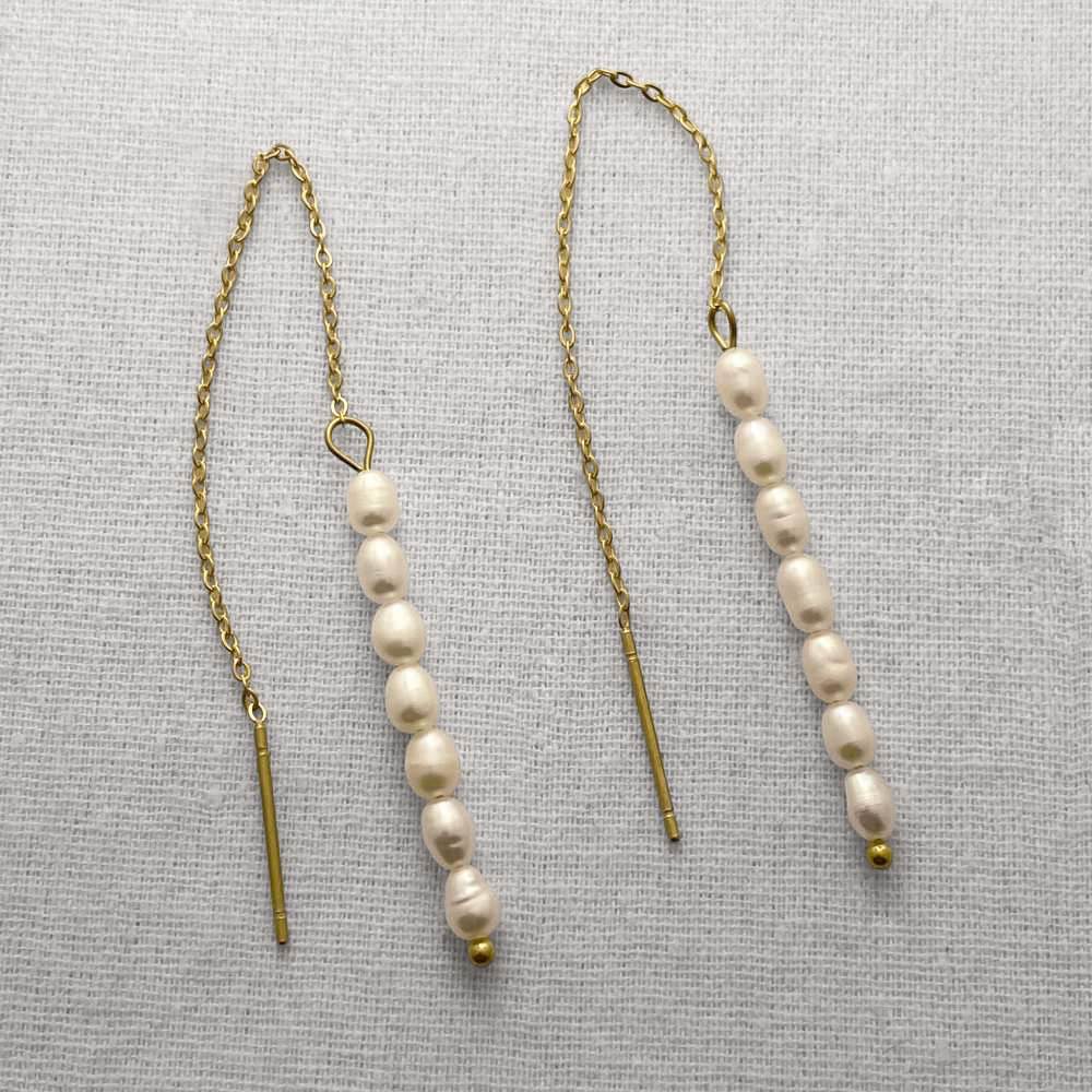 Pair of pearl threader earrings on a beige fabric background