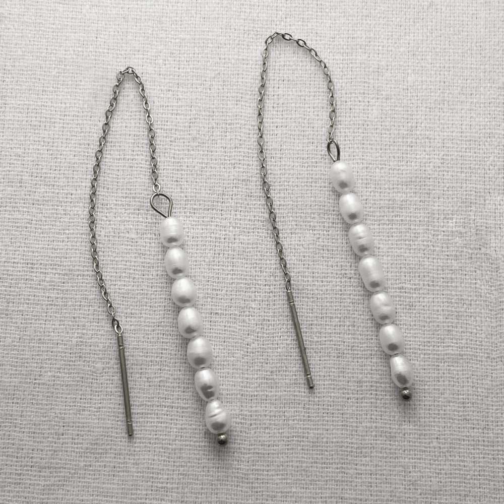 Pearl threader earrings on a textured gray surface