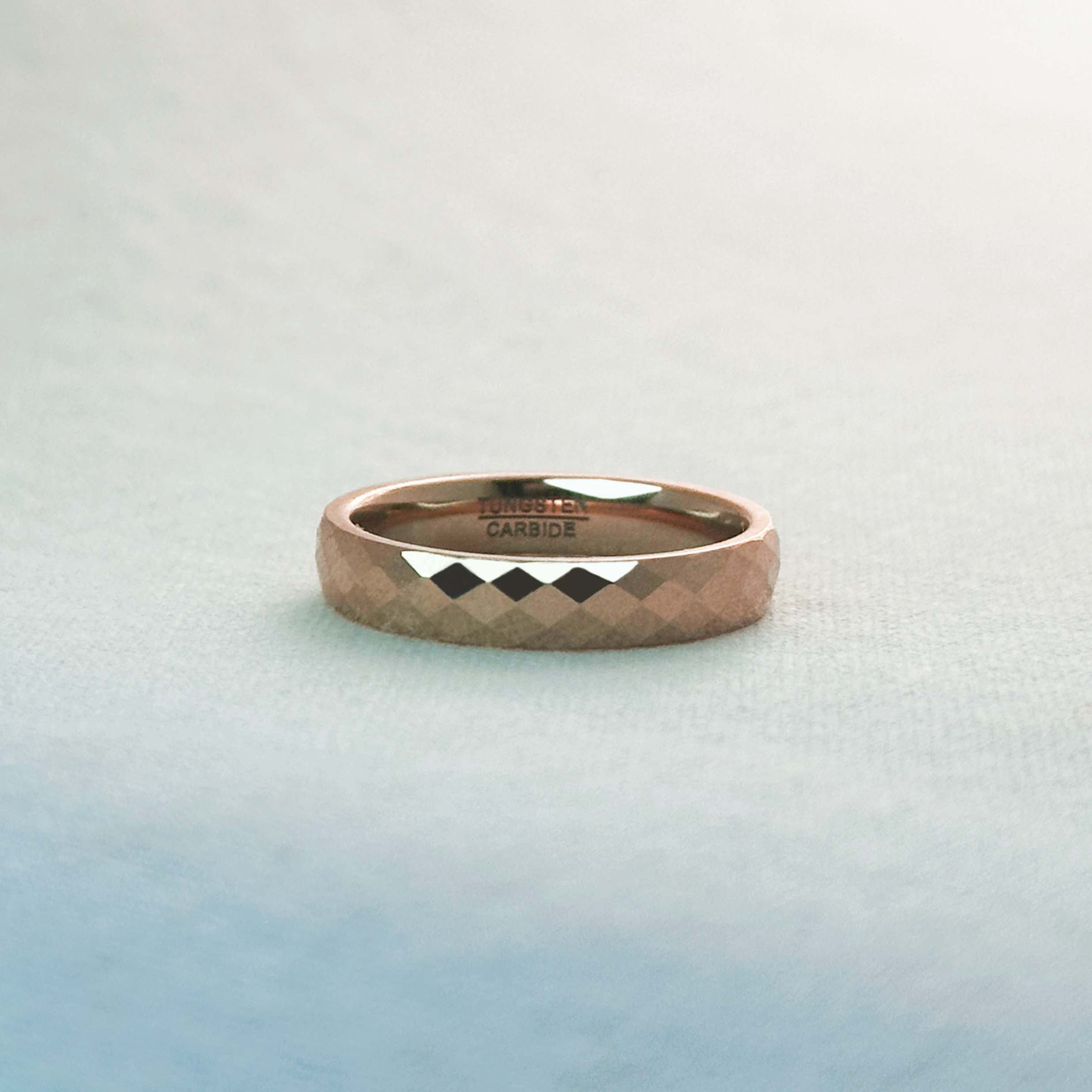 Rose gold ring with diamond pattern on a light blue gradient background