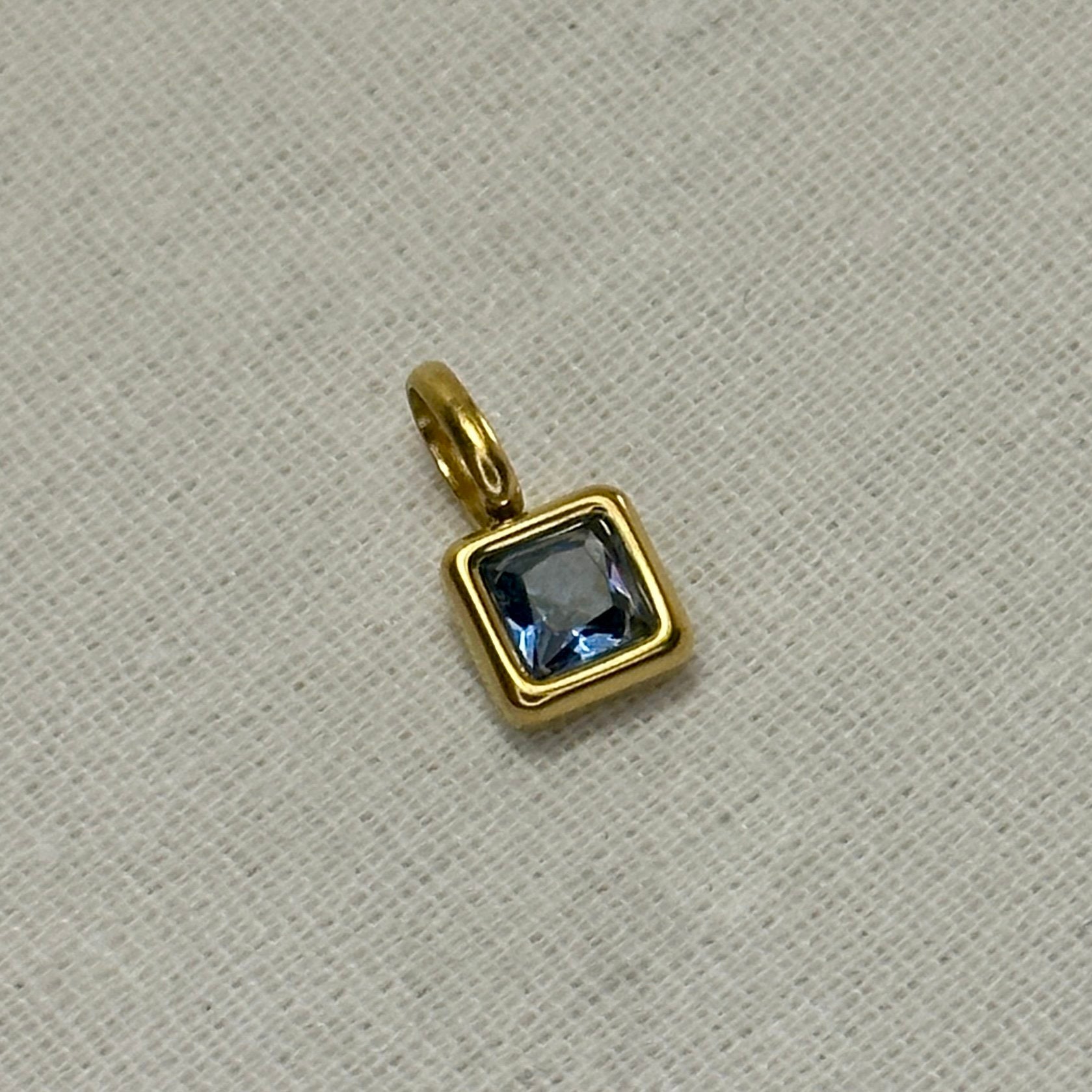 Gold pendant with a blue gemstone on a beige fabric background