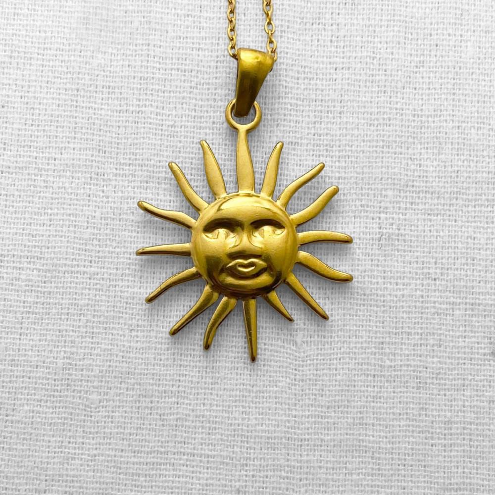 Gold sun-shaped pendant necklace on a beige fabric background