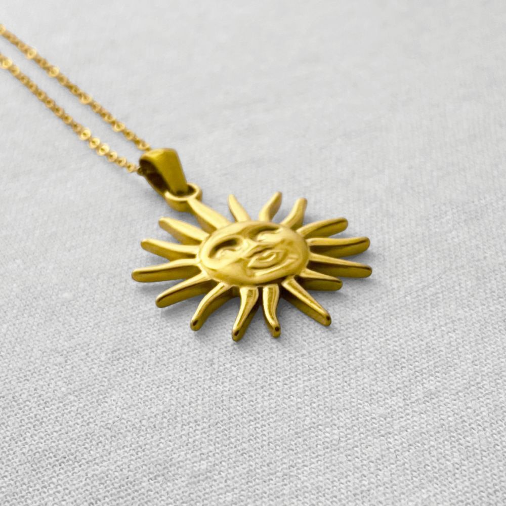 Gold sun-shaped pendant necklace on a beige fabric background