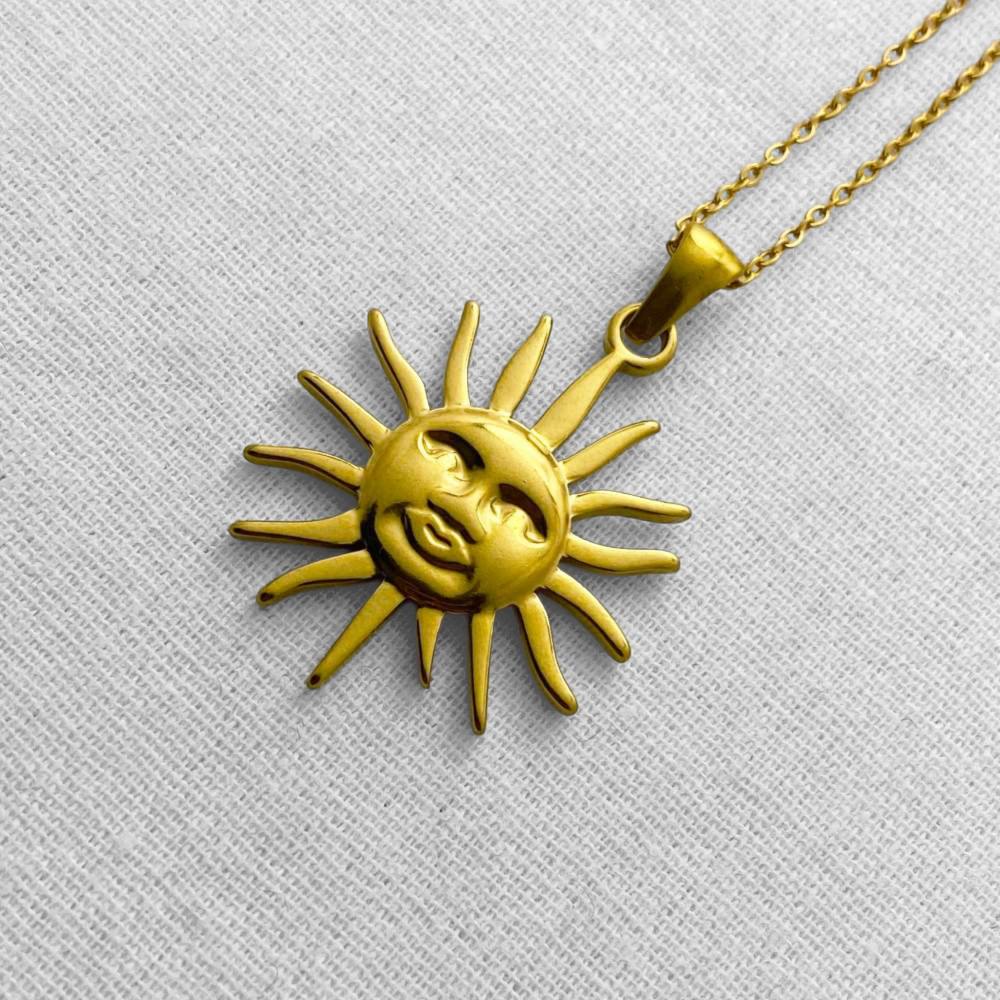 Gold sun and moon pendant necklace on a beige background