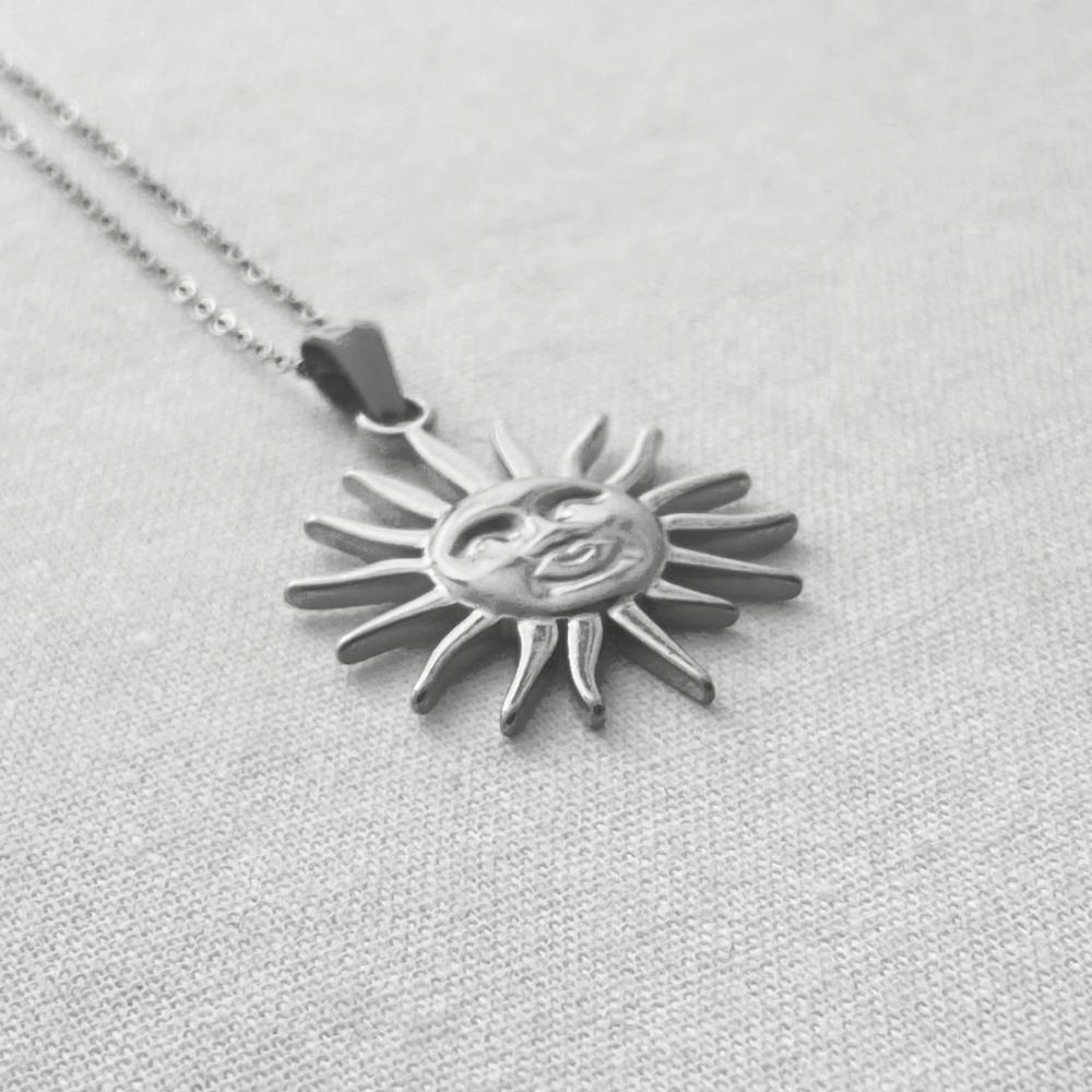 Silver sun-shaped pendant necklace on a light gray background