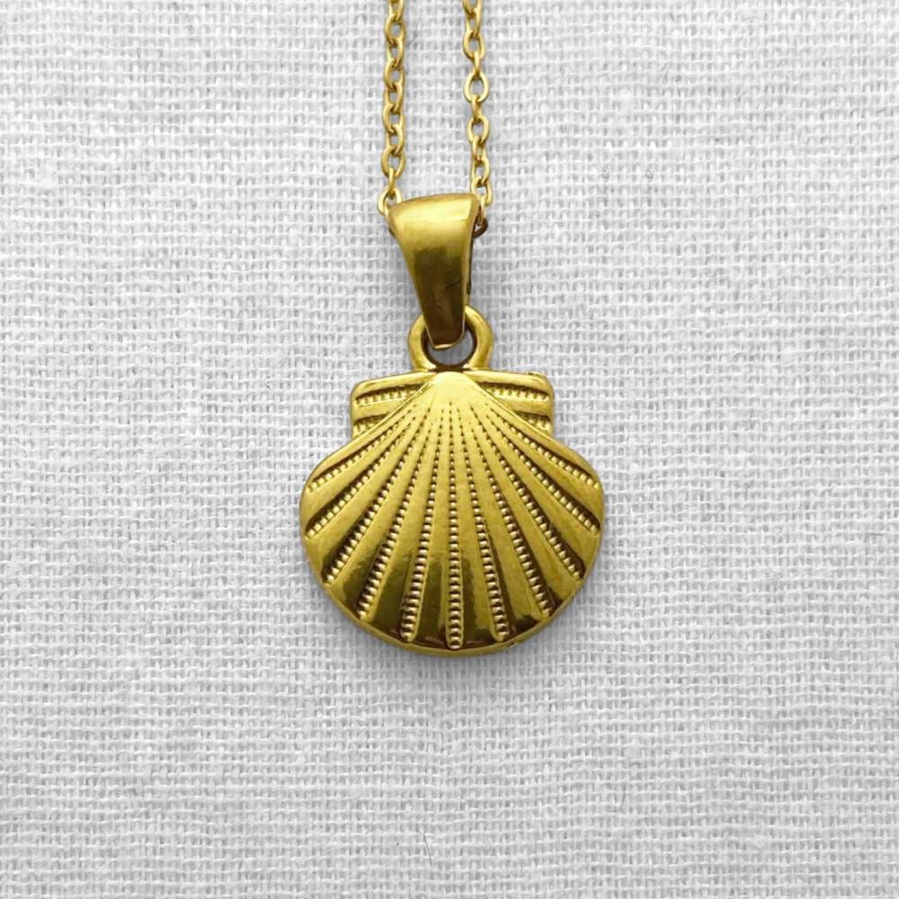 Gold shell pendant necklace on a beige fabric background