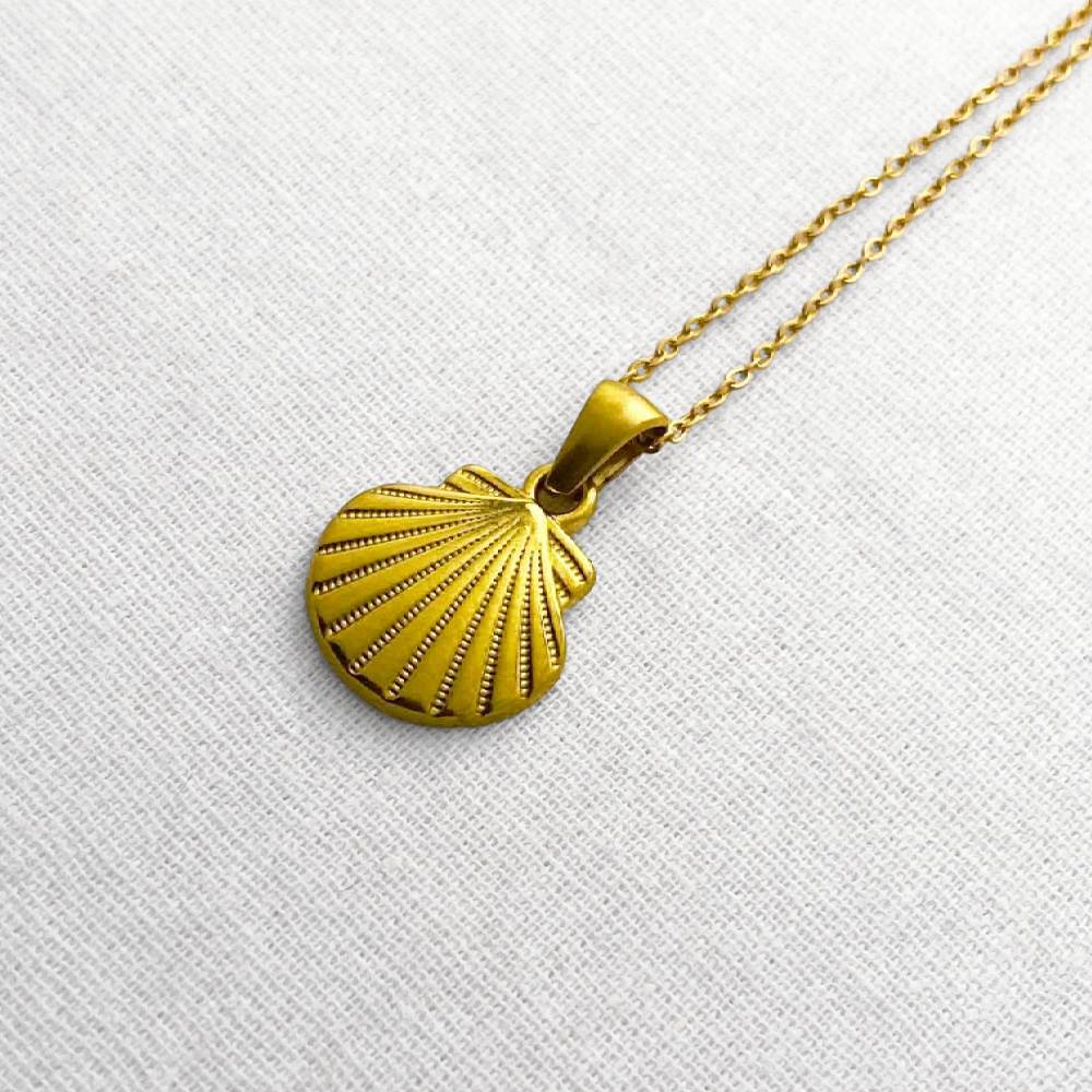 Gold shell pendant necklace on a beige fabric background