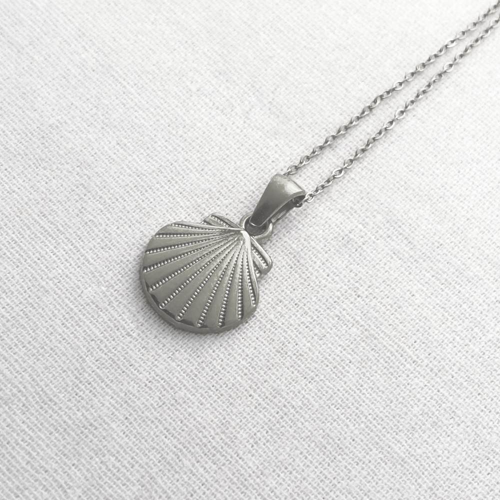 Silver shell pendant necklace on a light gray fabric background